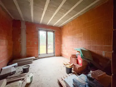 Pokój surowy z oknem tarasowym i materiałami budowlanymi na podłodze