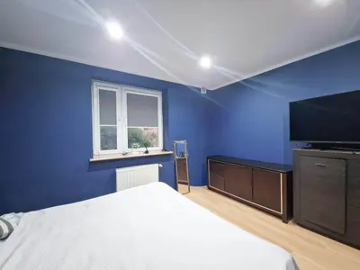 Sypialnia z niebieską ścianą, szafką RTV i telewizorem, parkiet