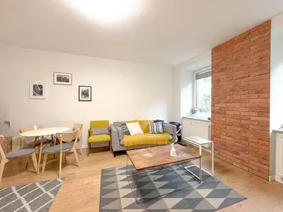 Salon z drewnianą podłogą, żółtą sofą, ceglaną ścianą akcentującą i jadalnią – Tuwima Łódź