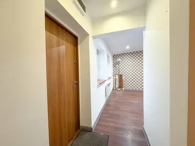 Przedpokój z drewnianą podłogą prowadzący do pokoju z kratowaną tapetą — kawalerka Łódź